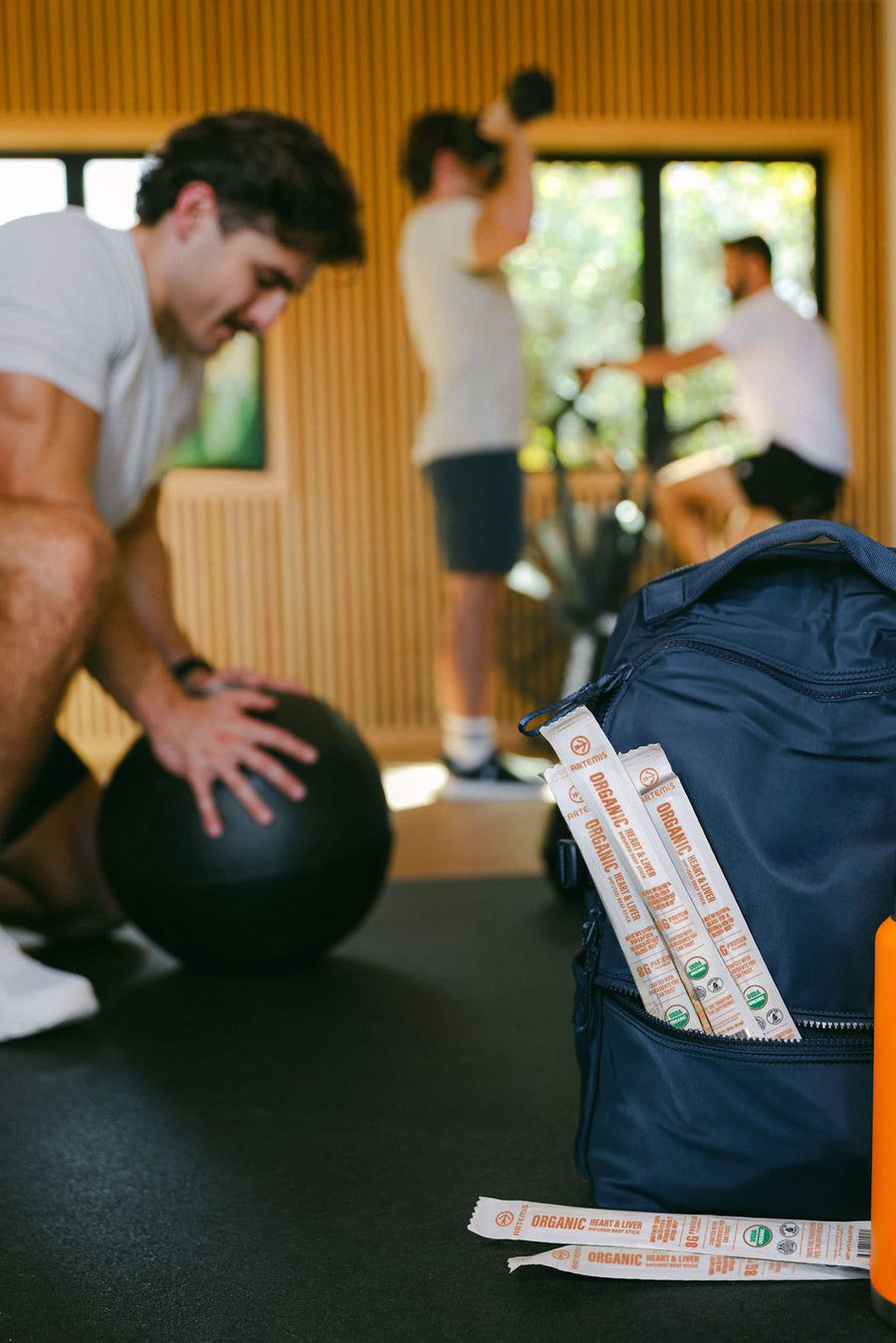 Artemis Heart & Liver beef sticks tucked into a gym bag beside a man working out with a medicine ball