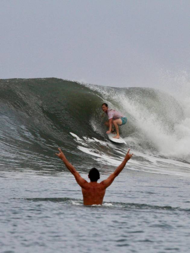 Surfer riding a wave while a swimmer in the foreground raises both arms