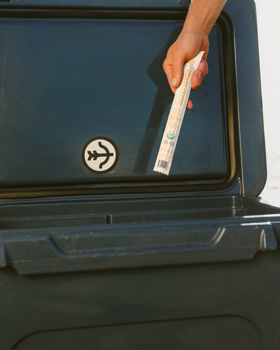 Man in a striped shirt lifting an Artemis beef stick from an open cooler on the beach