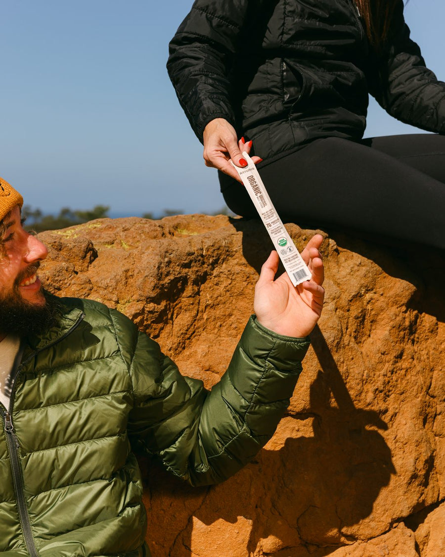 Man in a green jacket taking an Artemis Organic Original beef stick handed down from a red rock